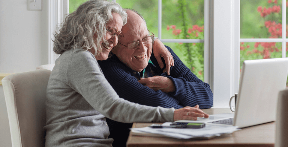 Seniorenpaar nutzt einen Laptop und informiert sich über spitex und lacht Zuhause
