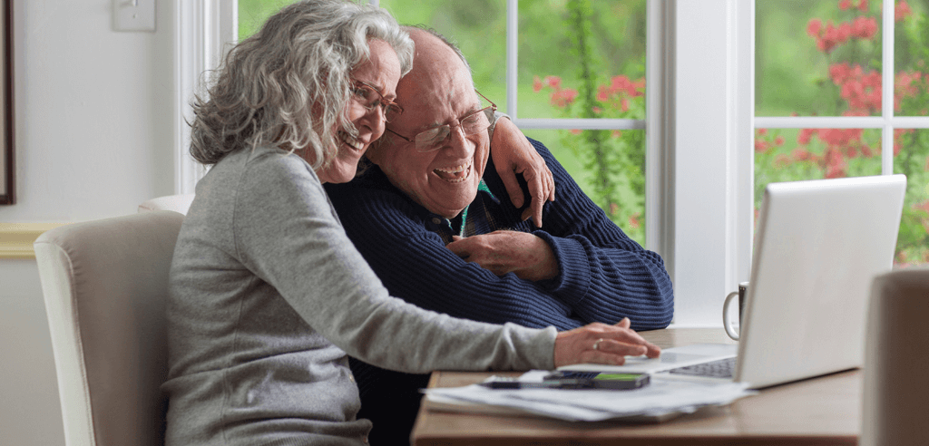 Seniorenpaar nutzt einen Laptop und lacht Zuhause