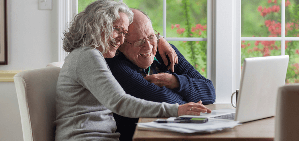 Seniorenpaar nutzt einen Laptop und lacht Zuhause