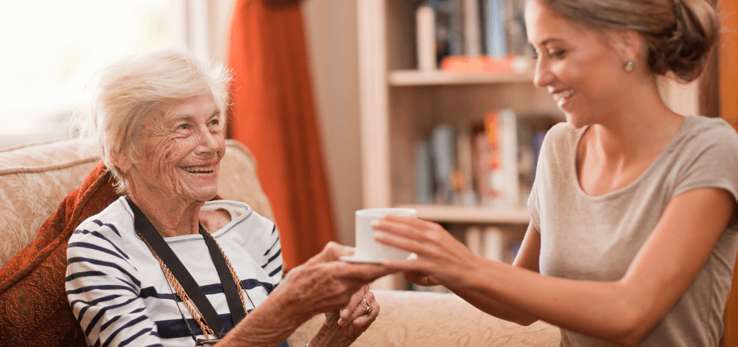 Pflegerin reicht Seniorin eine Tasse Kaffee