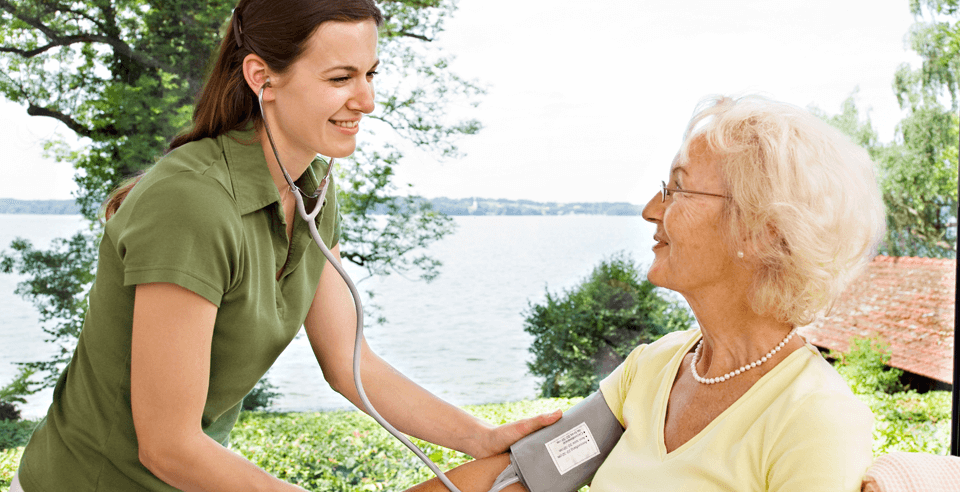 Pflegerin in der Ausbildung misst den Blutdruck einer Seniorin